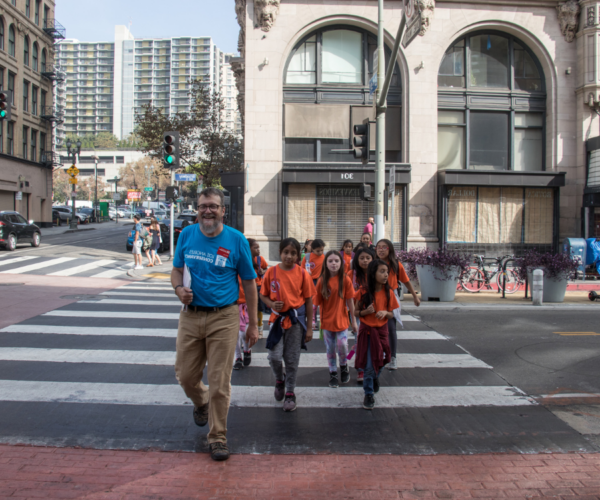 学生s in matching shirts cross a downtown street with a Conservancy tour guide.